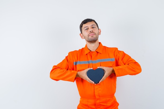 Gratis foto jonge werknemer die in eenvormige huidige doos houdt en zelfverzekerd kijkt.