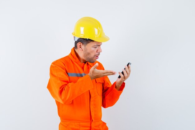 Jonge werknemer in uniform kijken naar mobiele telefoon en boos kijken.