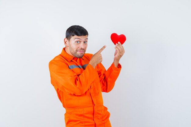 Jonge werknemer wijzend op rood hart in uniform en ziet er vrolijk uit.