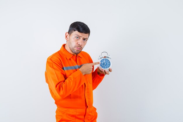 Jonge werknemer wijzend op wekker in uniform.