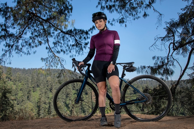 Jonge wielrenner poseert met haar fiets op een uitkijkpunt met een boslandschap op de achtergrond