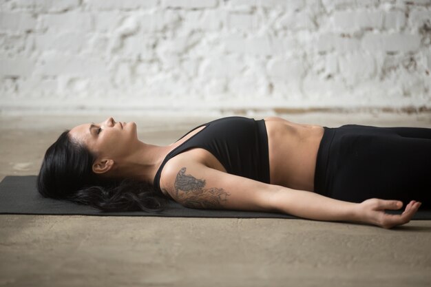 Jonge yogi aantrekkelijke vrouw in Savasana pose, loft achtergrond, c