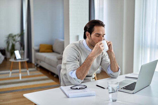 Jonge zakenman die geniet van een kopje koffie terwijl hij thuis aan de telefoon praat