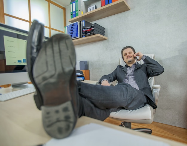 Gratis foto jonge zakenman die vanuit zijn kantoor werkt tijdens het gesprek aan de telefoon en ontspant