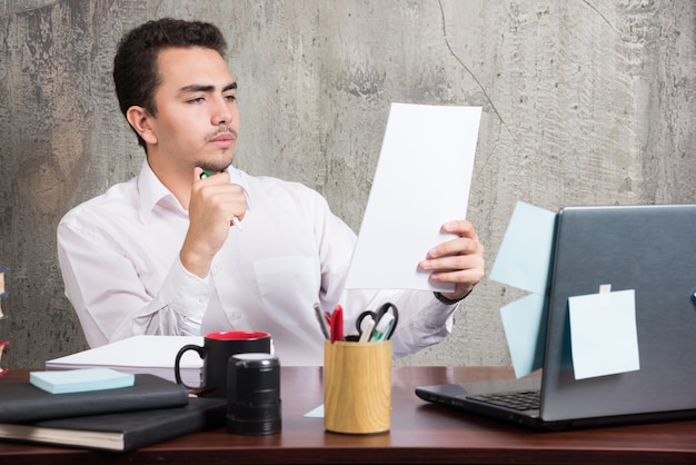 Jonge zakenman die werkdocumenten bij het bureau kijkt.