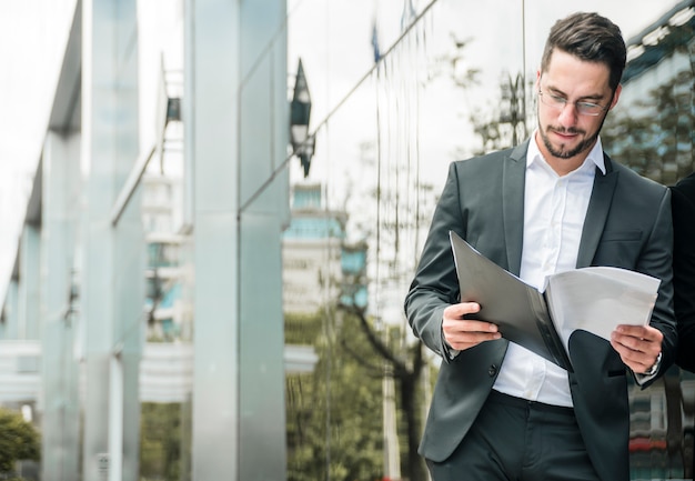 Jonge zakenman die zich bij in openlucht bevindt die het document leest