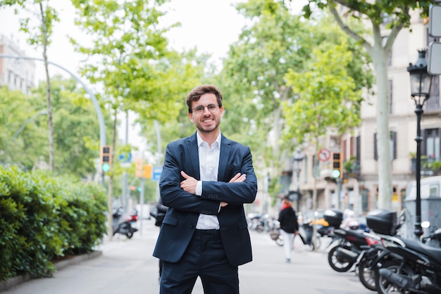 Jonge zakenman die zich op straat met zijn gekruiste die wapen bevinden camera bekijken