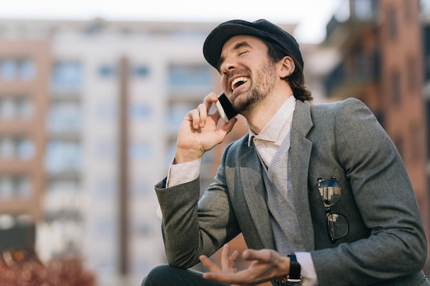 Gratis foto jonge zakenman lacht terwijl hij met iemand praat via een mobiele telefoon op straat