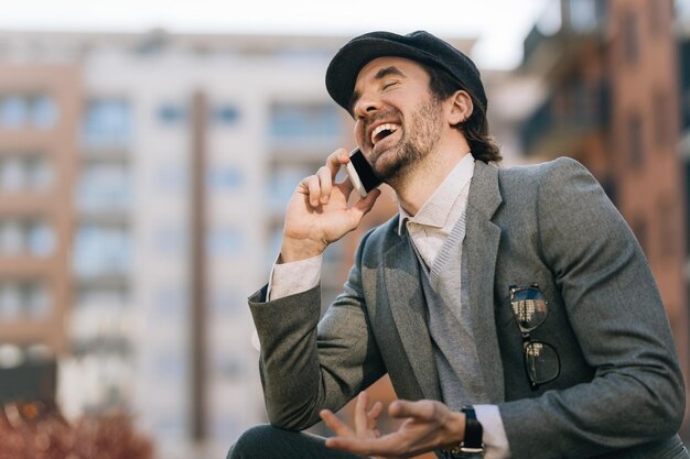 Jonge zakenman lacht terwijl hij met iemand praat via een mobiele telefoon op straat
