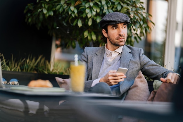 Jonge zakenman sms't op mobiele telefoon terwijl hij ontspant in een café en wegkijkt