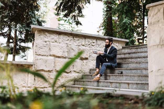 Jonge zakenman zittend op trap met behulp van laptop op park