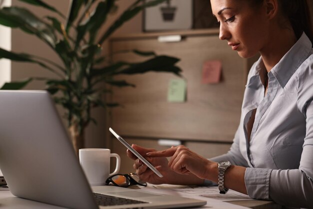 Jonge zakenvrouw die aan touchpad werkt en op het net surft op haar bureau