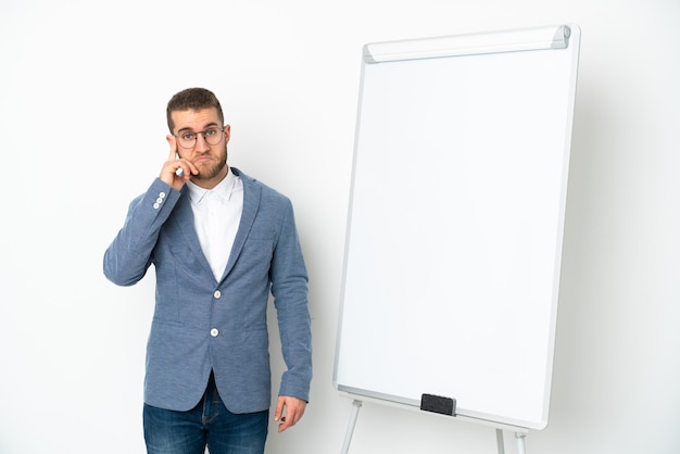 Jonge zakenvrouw die een presentatie geeft op een wit bord dat op een witte achtergrond wordt geïsoleerd en een idee denkt