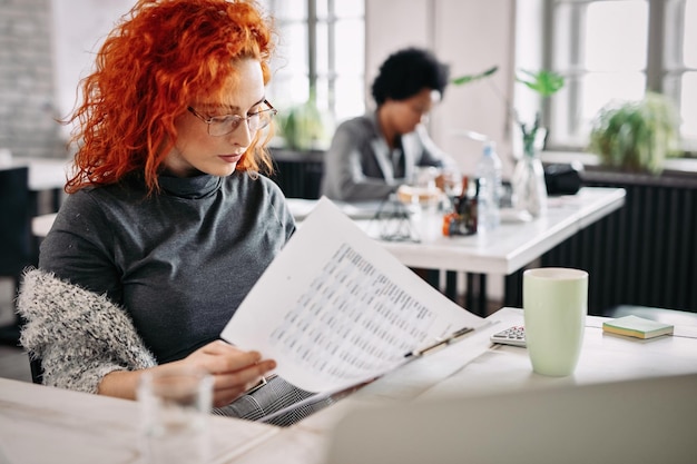 Jonge zakenvrouw die financiële rapporten leest terwijl ze op kantoor werkt