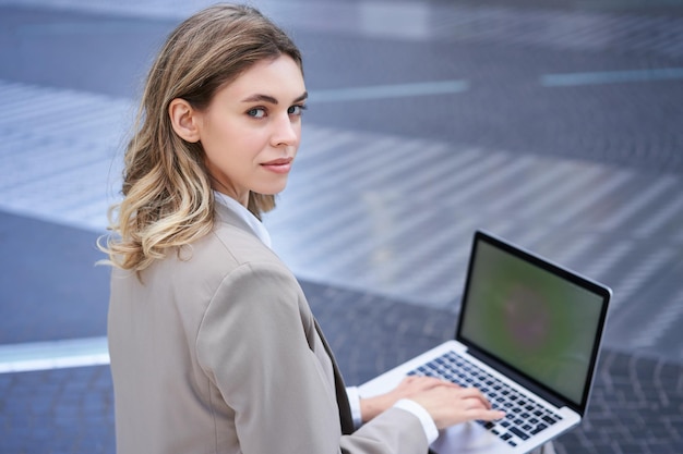 Jonge zakenvrouw die laptop gebruikt terwijl ze buiten in het stadscentrum zit te typen op toetsenbord meisje prepa