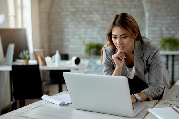 Jonge zakenvrouw die op een computer op het net surft terwijl ze op kantoor werkt