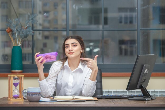 Jonge zakenvrouw die op kantoor zit en een koffiecontainer vasthoudt en er met een vinger naar wijst Hoge kwaliteit foto