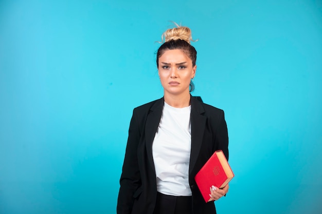 Jonge zakenvrouw in zwarte blazer met een boek en ziet er depressief uit.