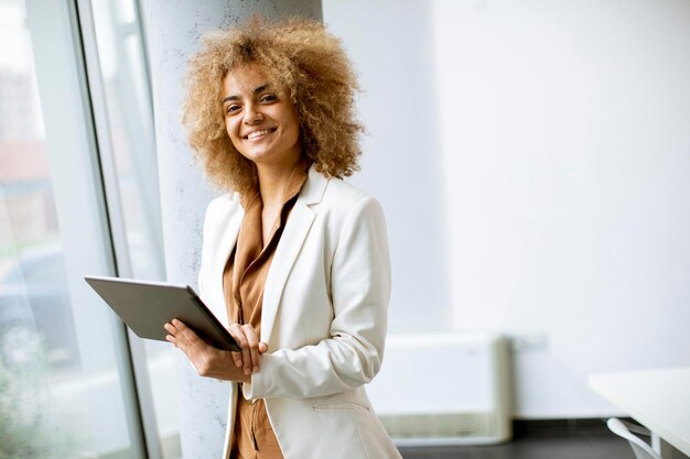Jonge zakenvrouw met krullend haar die digitale tablet op kantoor gebruikt met jonge mensen die achter haar werken