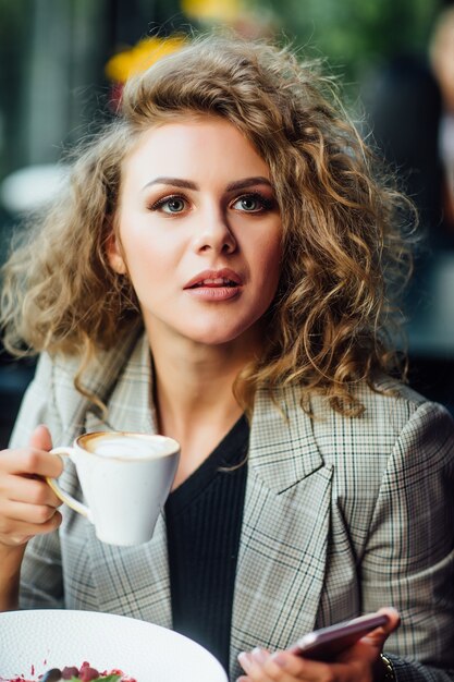 Jonge zakenvrouw rusten in restaurant met kopje latte en dessert op tafel.