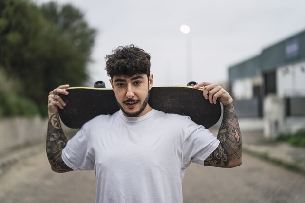 Jonge zelfverzekerde Europese man die een schaats vasthoudt op een wazige achtergrond van een straat