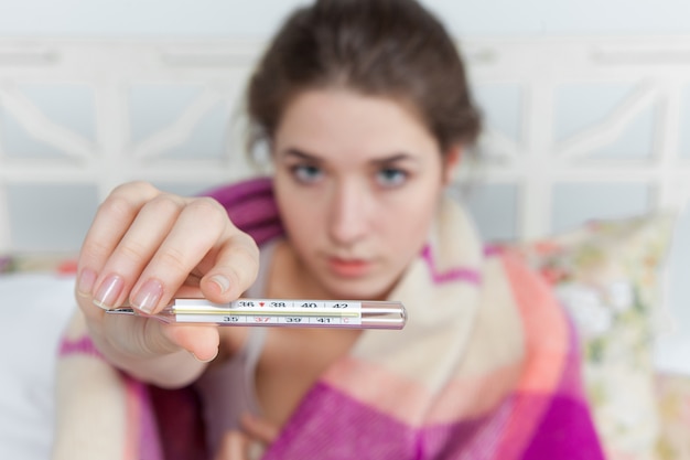 Jonge zieke vrouw in deken met thermometer