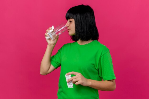 Jonge zieke vrouw met pak tabletten servet en glas water drinkwater geïsoleerd op roze muur met kopie ruimte