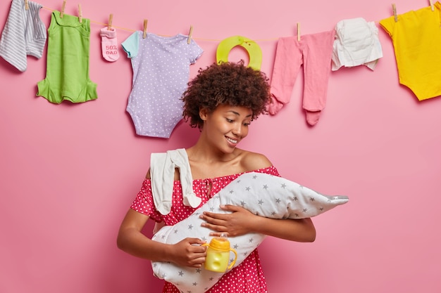 Jonge zorgzame moeder geeft om pasgeboren kind, voedt zich met melk, geniet van gelukkige momenten van moederschap, poseert thuis. Kleine baby op kunstmatige voeding. Oppassen, ouderschap concept. Bevalling