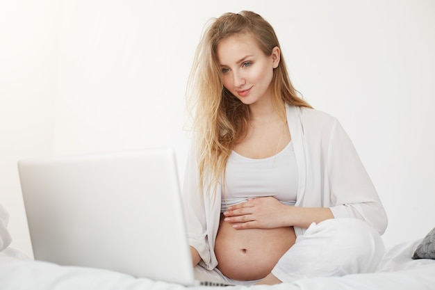 Jonge zwangere bedrijfsvrouw die haar online opslag van babykleertjes in werking stelt. Moederlijk ondernemerschap freelance thuiswerk.
