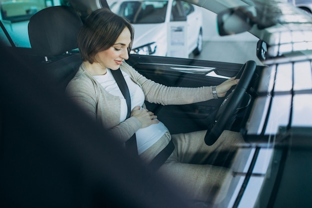 Jonge zwangere vrouw die een auto in autotoonzaal testen