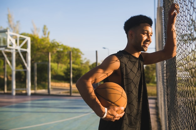 Jonge zwarte man sporten, basketbal spelen op zonsopgang, actieve levensstijl, zomerochtend