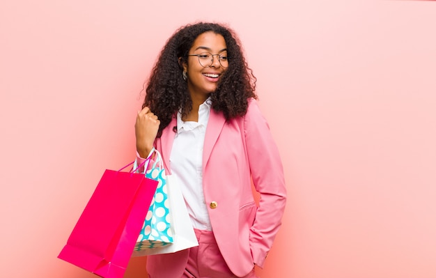 Jonge zwarte mooie vrouw met boodschappentassen tegen roze muur