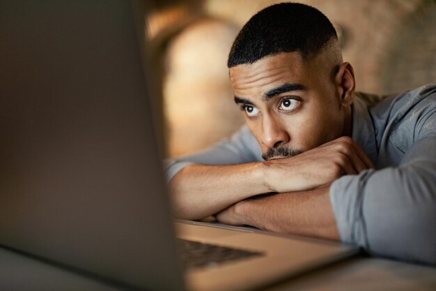 Jonge zwarte ondernemer leunt op zijn bureau terwijl hij 's nachts een e-mail leest op zijn laptop