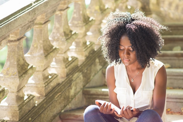 Jonge Zwarte Vrouw Lezen Boek Op De Trappen In Park