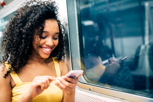 Gratis foto jonge zwarte vrouw zit in de metro op de mobiele telefoon