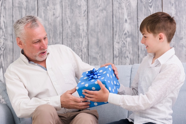 Jongen die de blauwe verpakte doos van de verjaardagsgift geeft aan zijn grootvader