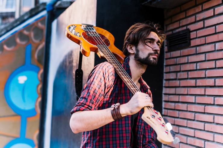 Gratis Foto jongen die de elektrische gitaar naast bakstenen muur houdt