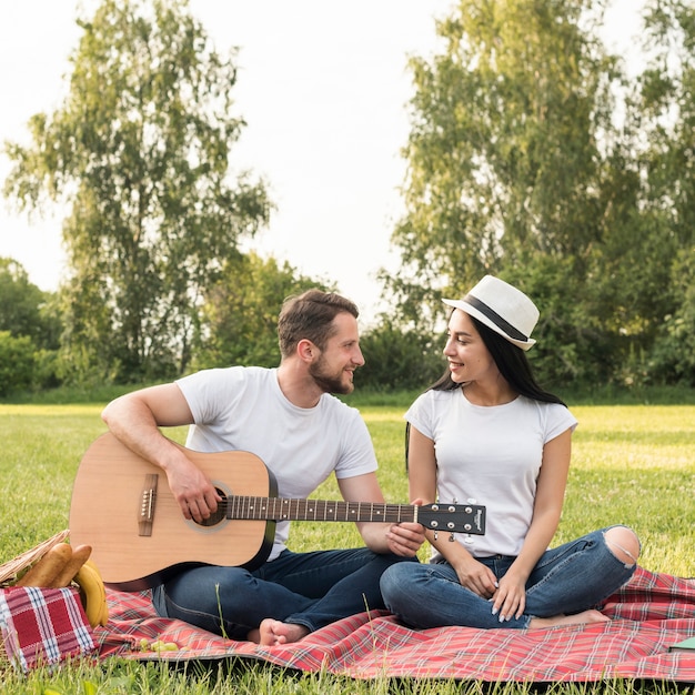 Jongen die de gitaar voor zijn meisje op een picknickdeken speelt