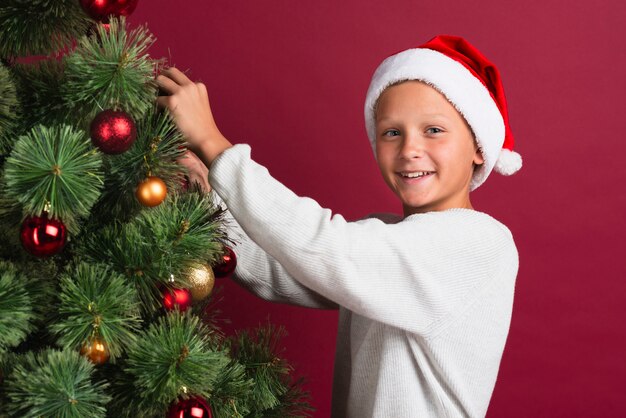 Jongen die het middelgrote schot van de Kerstmisboom verfraait