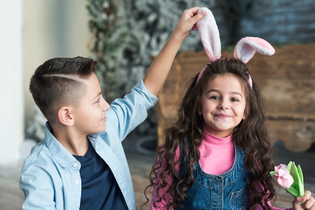 Gratis foto jongen die meisje in konijntjesoren bekijkt met tulp