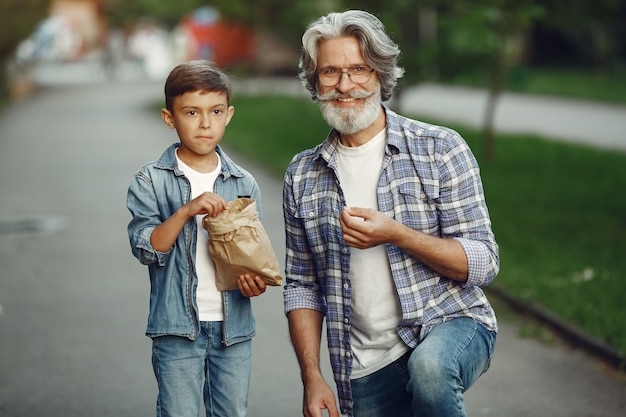 Jongen en grootvader wandelen in het park. Oude man speelt met kleinzoon. Mensen eten popcorn.