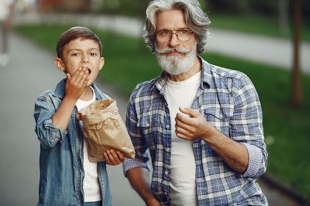 Jongen en grootvader wandelen in het park. Oude man speelt met kleinzoon. Mensen eten popcorn.