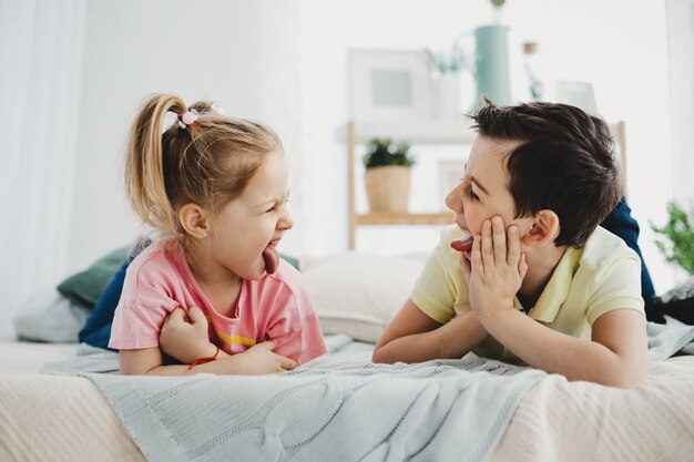 Jongen en meisje grimassen naar elkaar liggend op het bed