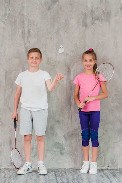 Jongen en meisjesspelers met rackets en shuttle tegen concrete achtergrond