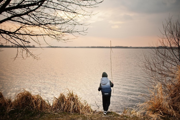 Jongen in hoodie bij het meer met een riet in zijn handen