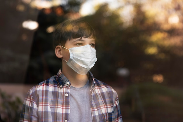 Gratis foto jongen met gezichtsmasker bij het kijken naar buiten door de ramen