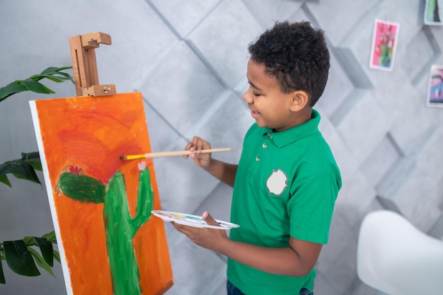 Gratis foto jongen wat betreft tekening op schildersezel met penseel