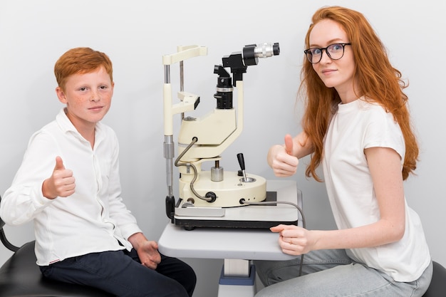 Jongens geduldige en vrouwelijke oogarts die duim op gebaar in optiekkliniek tonen