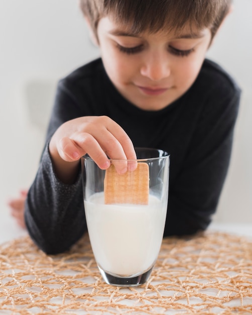 Jongens onderdompelend koekje in melk