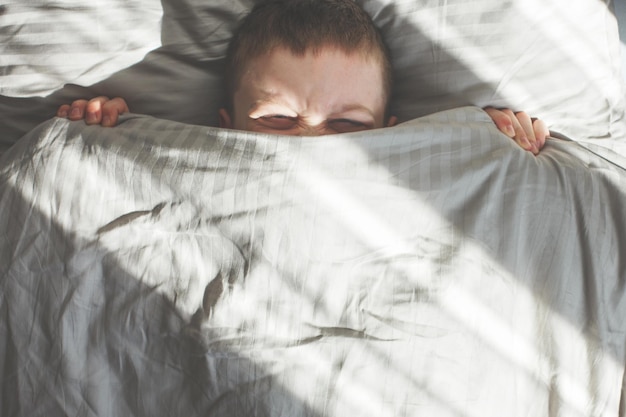 Jongensslaap in het bed. het kind ligt op een kussen en bedekt zijn gezicht met een deken